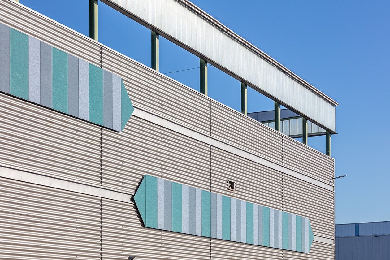 Buitenmuur met gekleurde pijlvormige panelen op een helderblauwe dag.